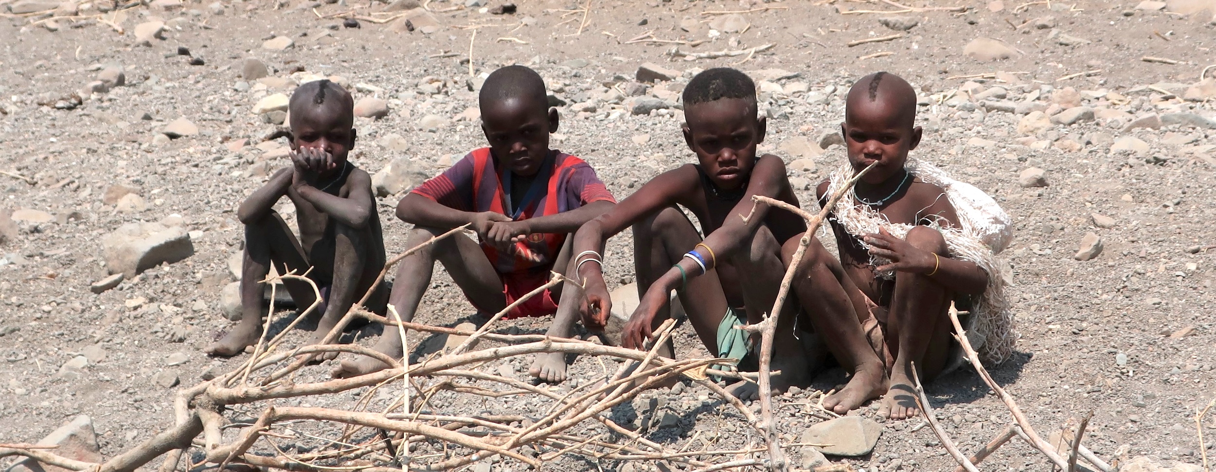 Four Himba children sitting in a row.